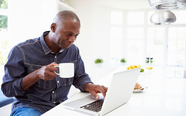 A man sits at a computer holding a mug