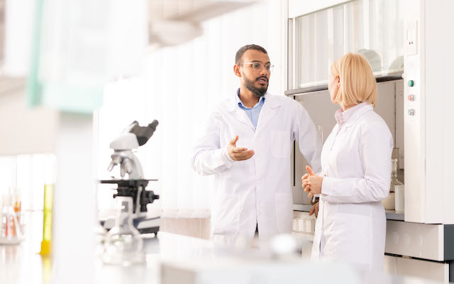 Two doctors in white coats converse in a lab