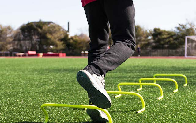 Man stepping over yellow mini banana hurdles on a field