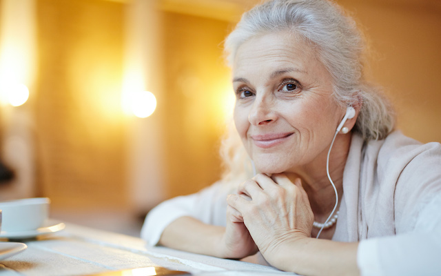 An older woman smiles to the distance with earphones on