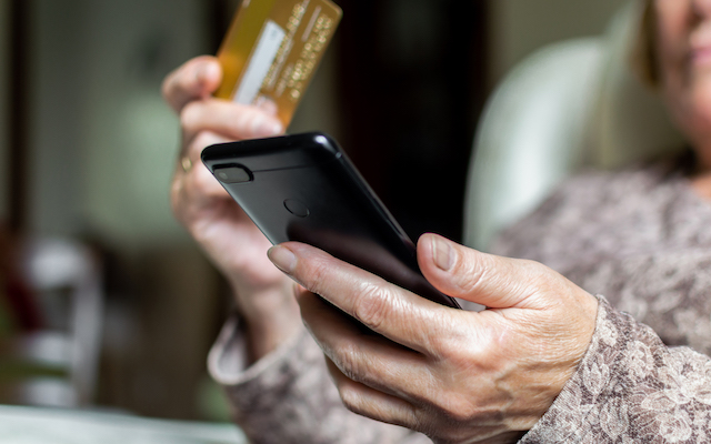 Old woman shopping online using a credit card and a smartphone at home