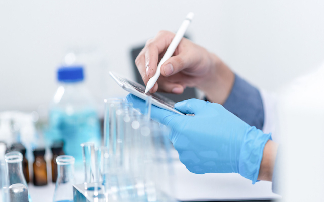 A clinician in a lab writes a note on a tablet.
