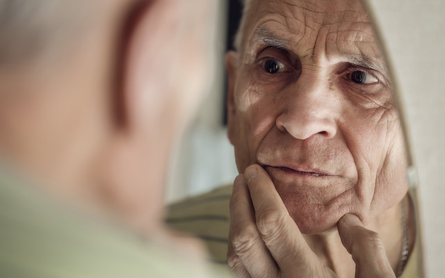 An older man looks closely at himself in the mirror.