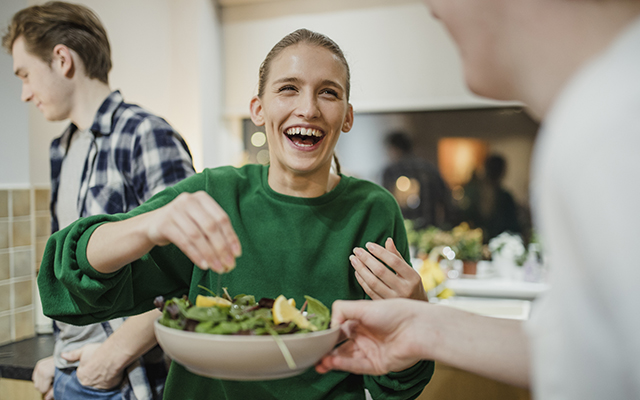 A women seasons a salad with friends.