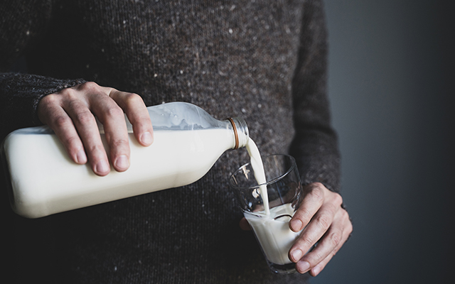front view closeup of young Caucasian man hands in dark wool pouring milk into a glass