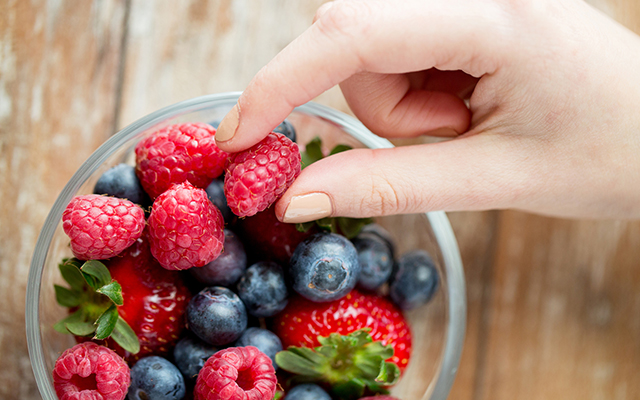 close up of woman hands with berries in glass bowl