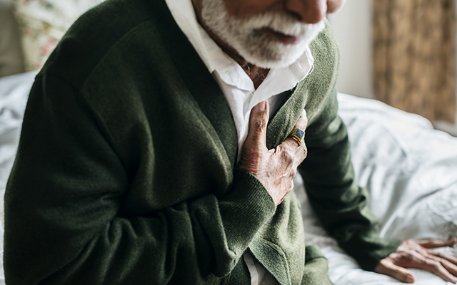 An elderly Indian man clutches his heart.
