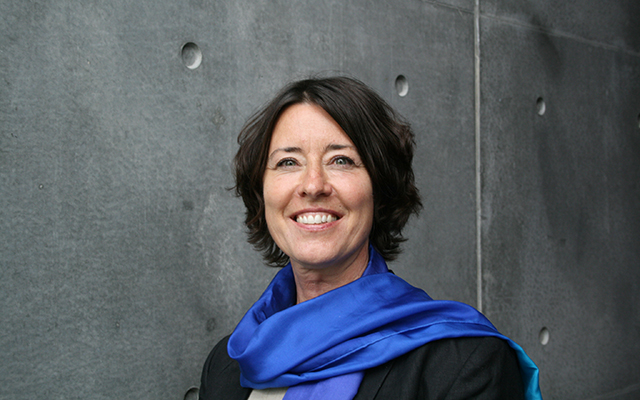 Dr Tove Henriksen wearing a blue scarf posing in front of a grey background.