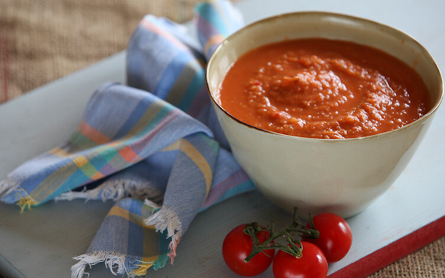 tomato and lentil soup in a white bowl, placed on a white board with three cherry tomatoes on the side