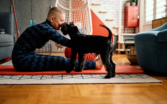 A man sitting up doing exercise on a yoga mat, with a black dog by his side
