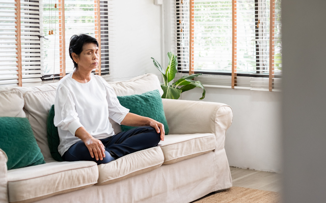 A woman sitting on a white sofa sitting crossed legged with her eyes closed