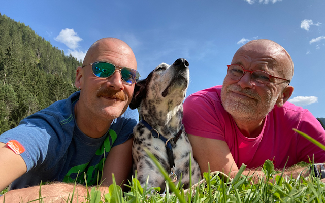 A photo of Peter Schielzeth sitting with his husband Daniel and their dog Basti.