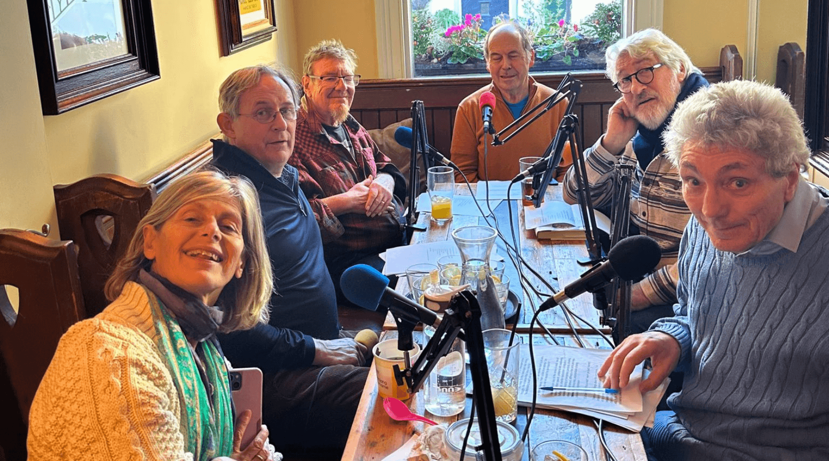 The cast of the Movers and Shakers Podcast sat around a table recording a podcast in a London pub