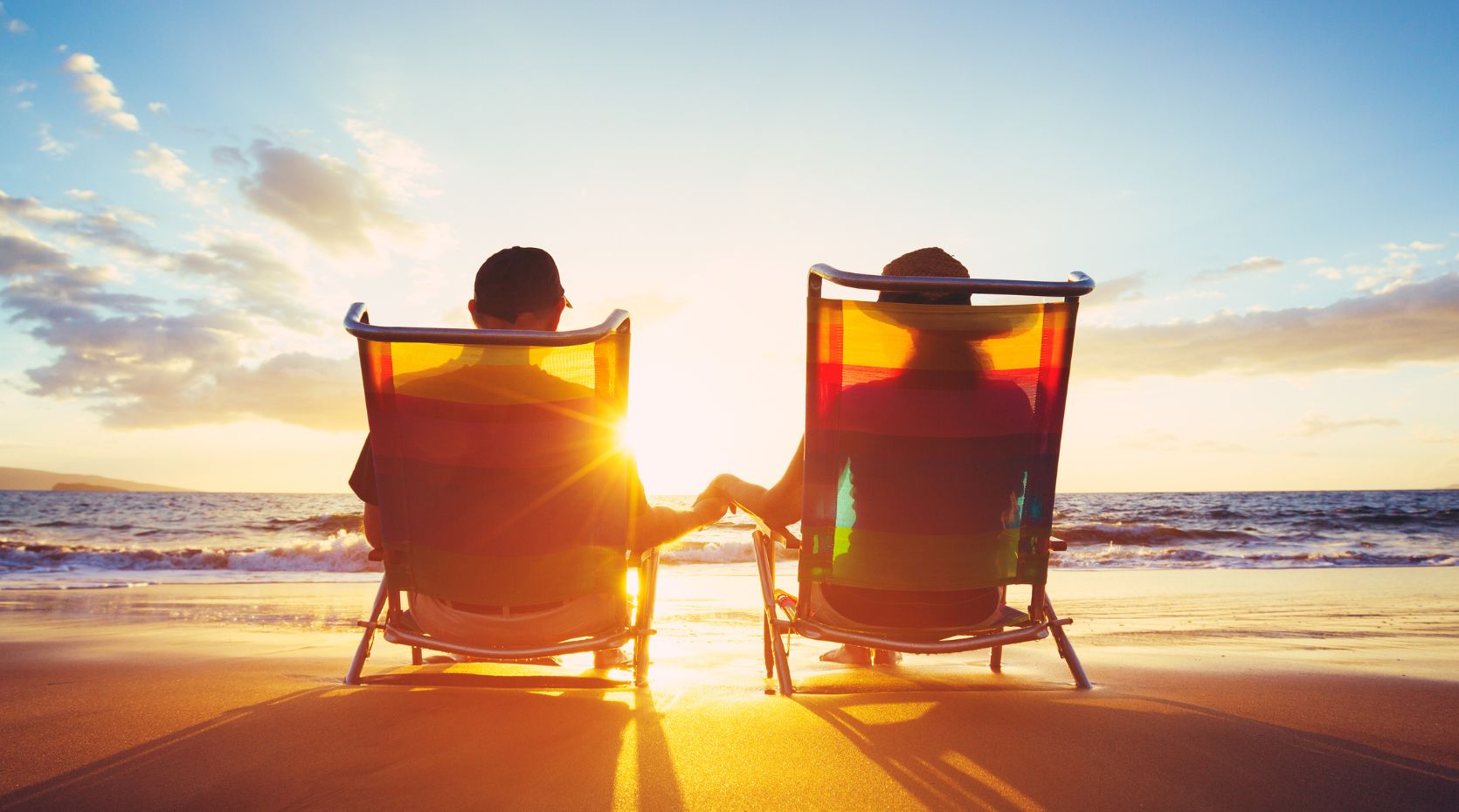 Parkinson's-friendly holidays represented by a couple sitting on deckchairs on the beach at sunset