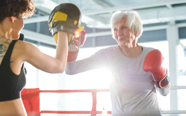 An older woman practices boxing with a trainer.