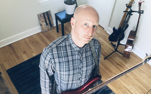 Robbie Tucker poses for a photo in a studio with a bass.