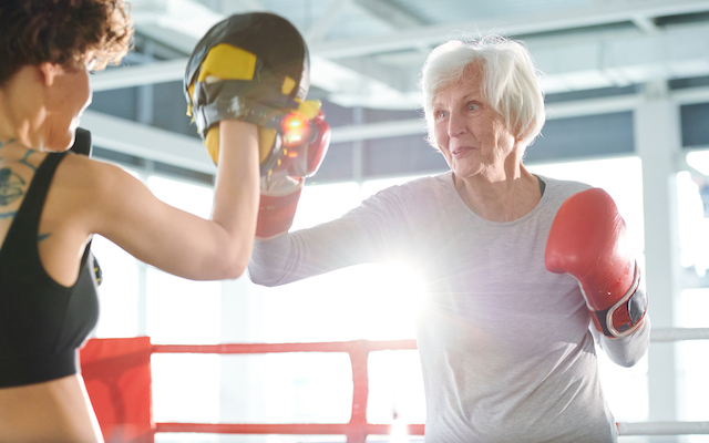 Senior white-haired woman in activewear and boxing gloves fighting with rival while training before competition