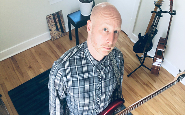 Robbie Tucker stands in his studio with a guitar.
