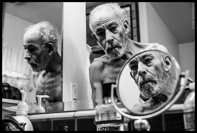 An image of Aly Shabaik looking at his reflection in a mirror.