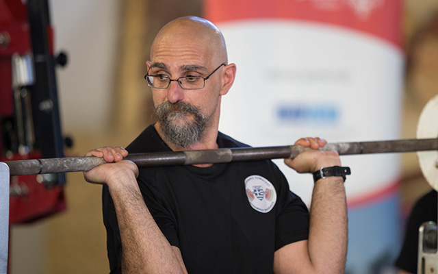 Nikolas powerlifting, while wearing glasses and a black t-shirt.