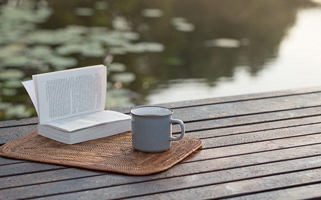 Book on a table next to a mug with a river in the background