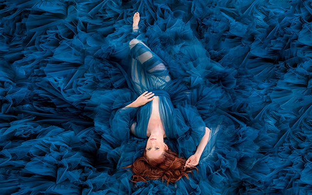 Caitlin Nagy laying down wearing a blue dress with blue material around her
