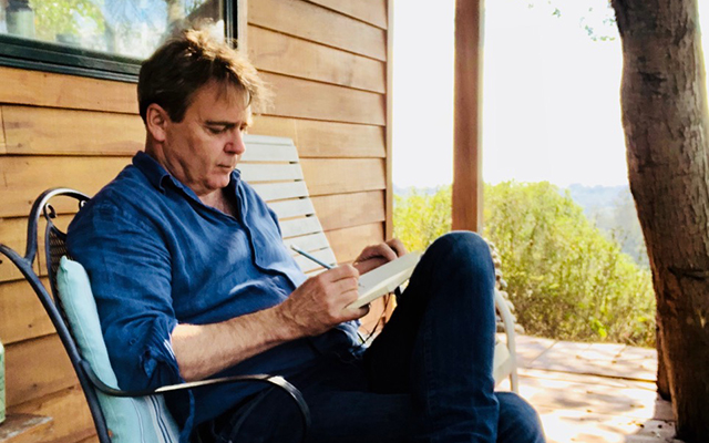 Marc Woodward sitting on a chair writing in a book