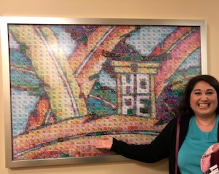 Dr Maria de Leon standing in front of a puzzle on display in a frame.