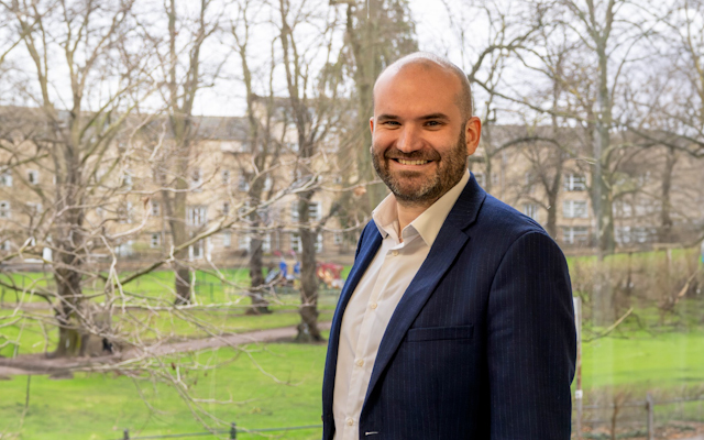 Dr Alistair Mackett in front of a tree-filled park. 